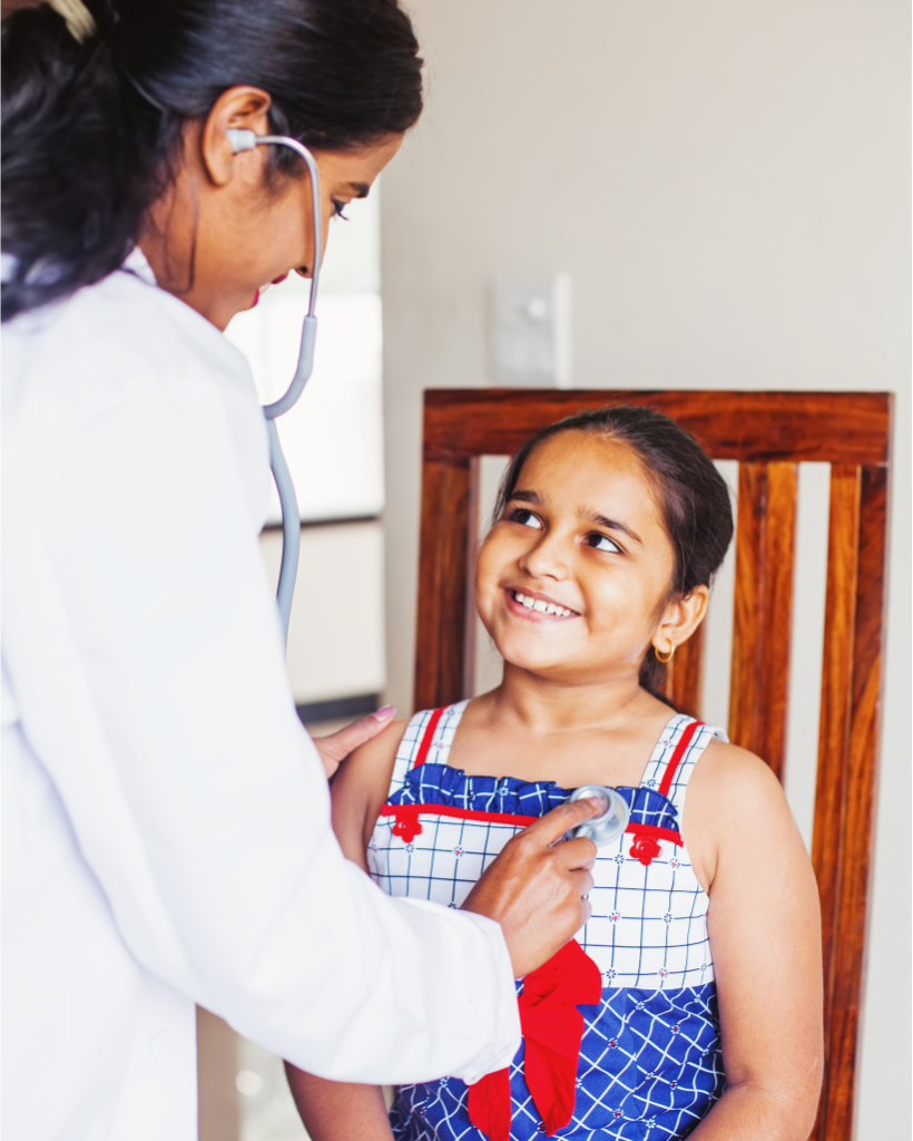 Smiling female doctor using a stethoscope to check the heartbeat of a young girl in a colorful dress.